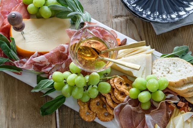 Cheese board with honey, grapes, pretzels, bread, prosciutto and cheese.