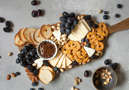An assortment of crackers, pretzels, baguette bread with fruit, nuts, cheese and fig jam.