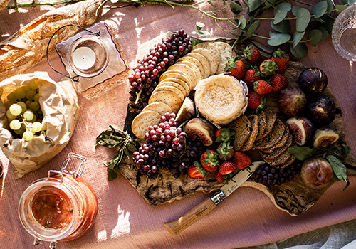 Washed-rind cheese on a board surrounded by crackers, grapes, strawberries and figs.