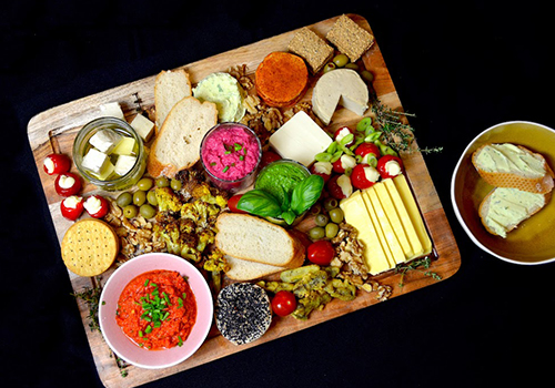 Vegan cheese board with dairy-free cheeses, breads, roasted cauliflower and dips.