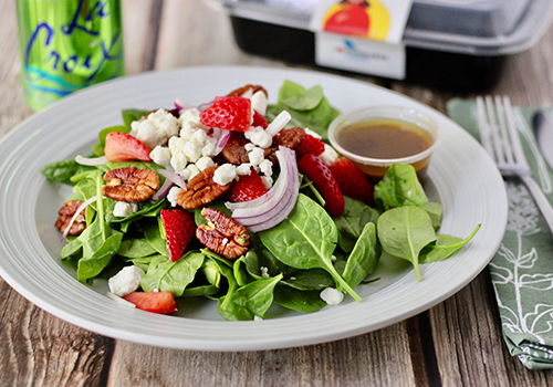 A plate of summer salad with strawberries, feta, pecans, onion and baby spinach.