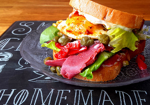 Pastrami sandwich with fried egg, capers, roast capscium and lettuce.