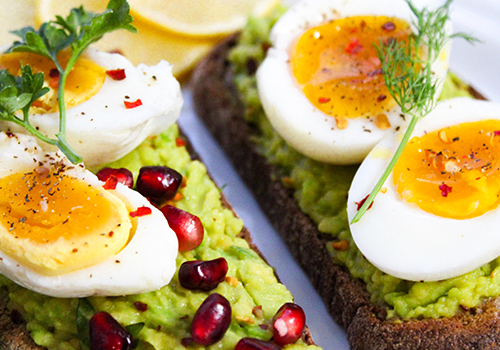 Smashed avocado on toast with jammy egg and pomegranate arils.