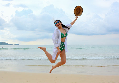 Woman in sunglasses, hat and jacket staying sunsmart at the beach.