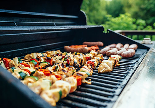 A wide BBQ with vegetarian kebabs and sausages.