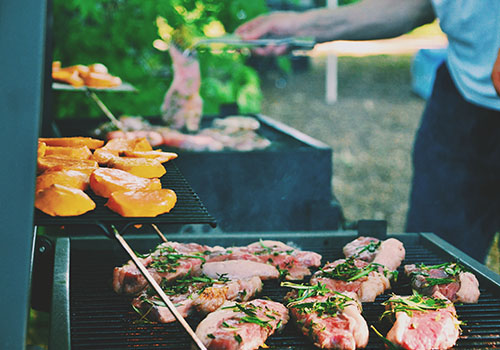 Shot over a number of different barbecue grills with steak and herbs, mango slices and fish.