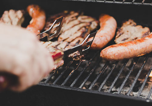 BBQ tongs turning meat on the grill.