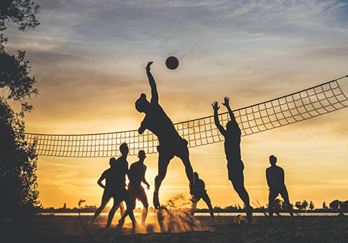 People playing beach volleyball at sunset